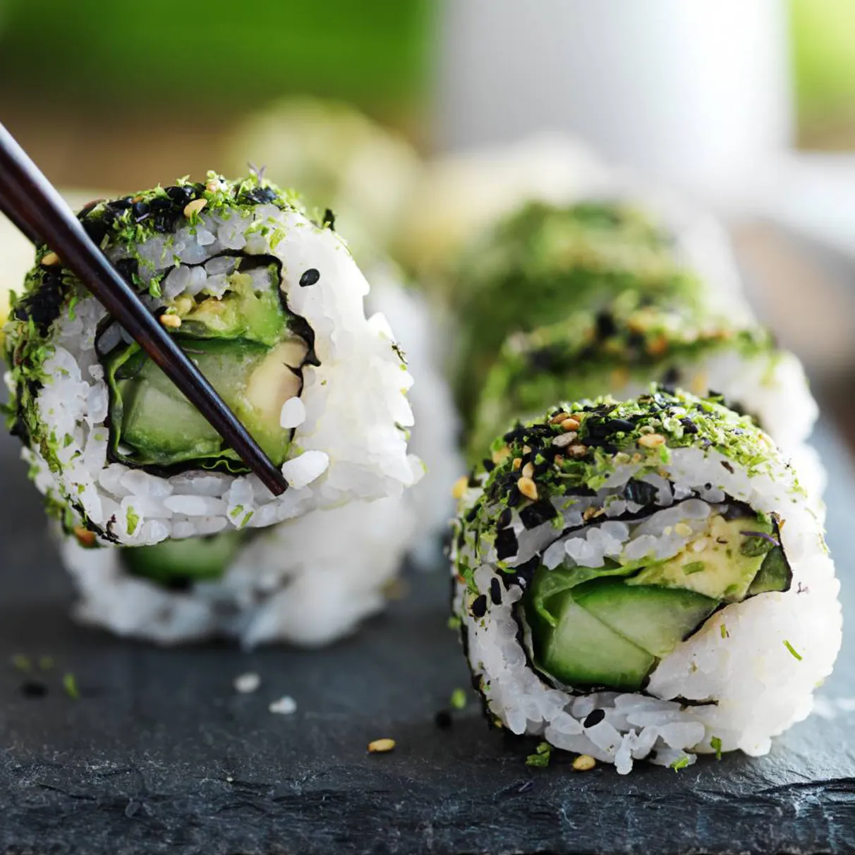 Cucumber and avocado sushi roll held with chopsticks