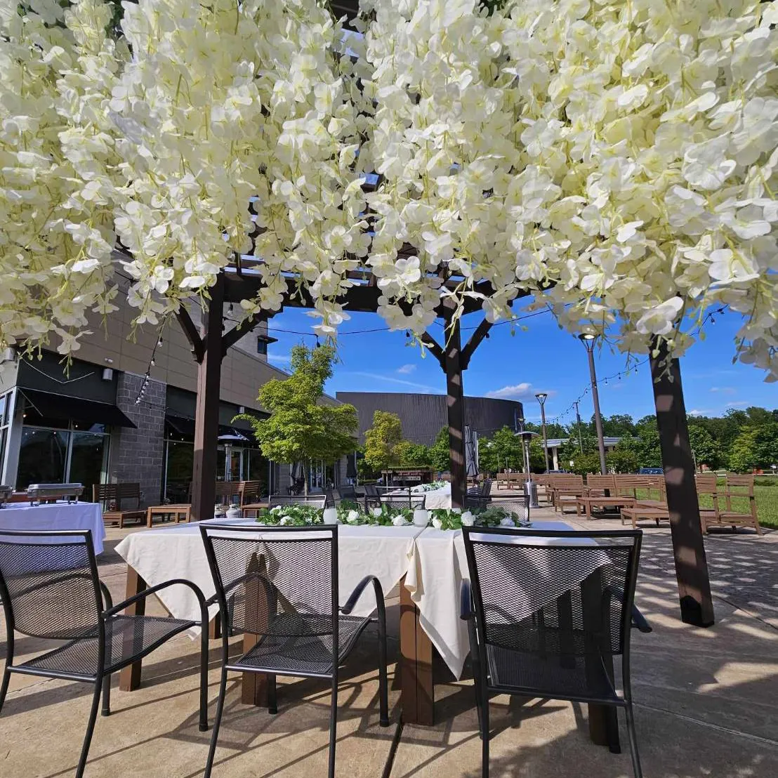 Patio tables set for an event under a canopy of white flowers